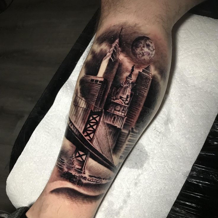 a man's arm with a black and grey city scene on the side of his leg