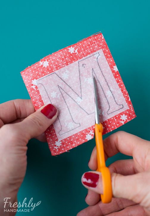 someone cutting out the letter m from a piece of paper with a pair of scissors