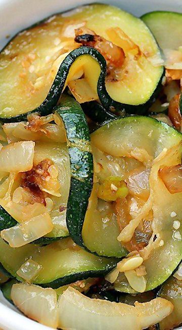 a white bowl filled with sliced zucchini and other vegetables on top of a table