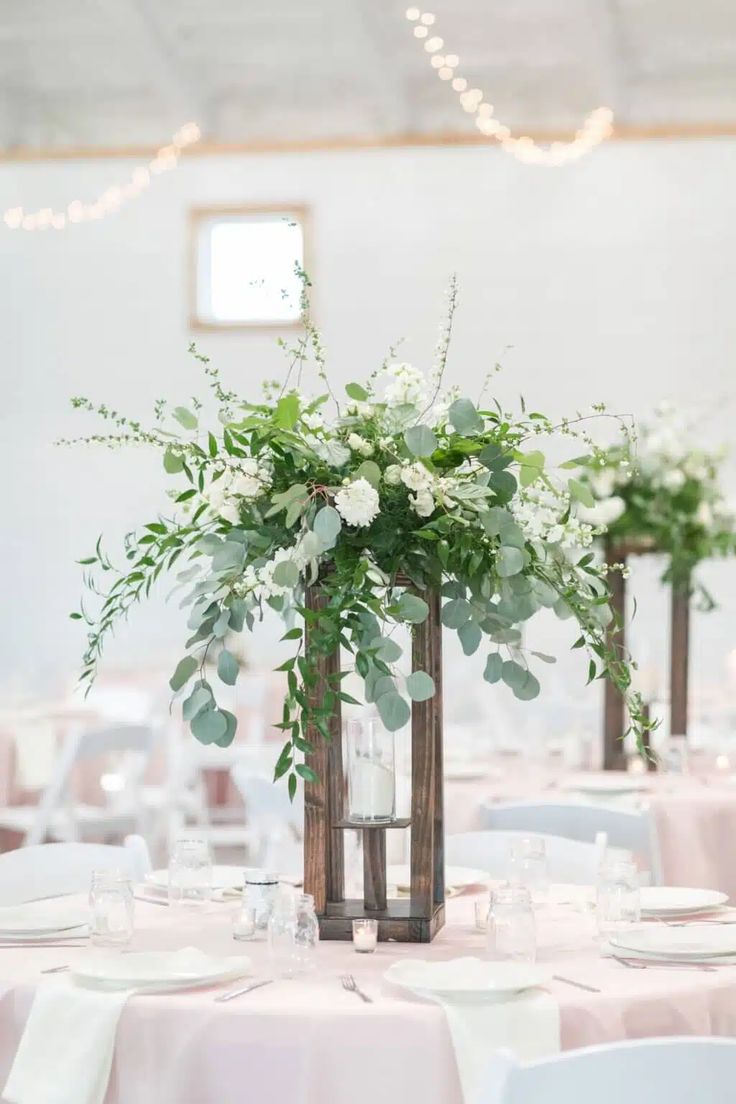 two tall vases filled with white flowers and greenery on top of a table