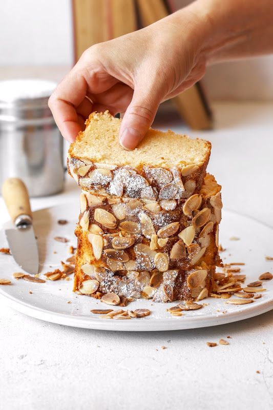 a person is picking up some kind of cake on a plate with almonds and powdered sugar