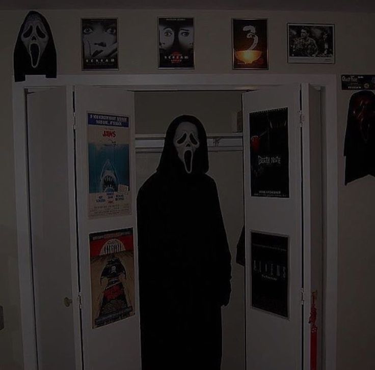 a person wearing a mask standing in front of a door with posters on the wall