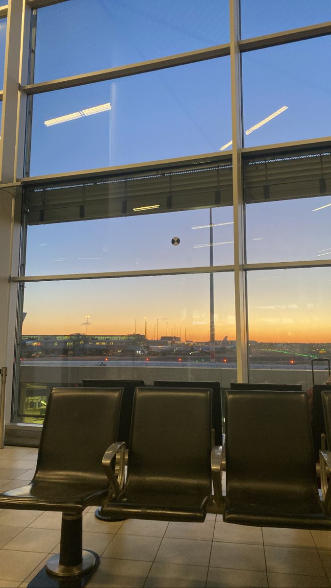 two empty chairs sitting in front of a window with the sun going down on an airport