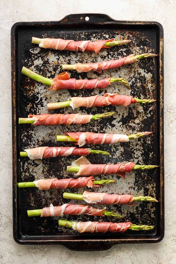 raw asparagus wrapped in prosciutto on a baking sheet, ready to be cooked