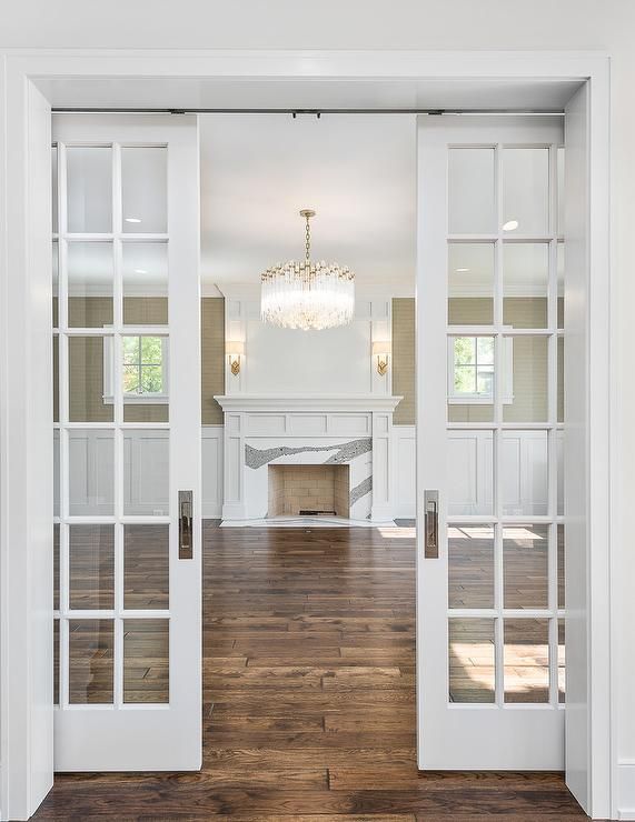 an open door leading to a living room with fireplace and chandelier in the background