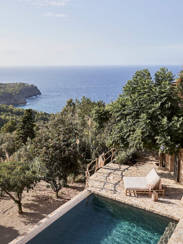 an outdoor swimming pool surrounded by trees next to the ocean with a lounge chair on it