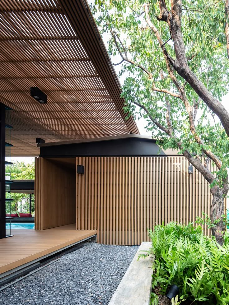 an outdoor area with plants and trees near a building that has a wooden wall on the side