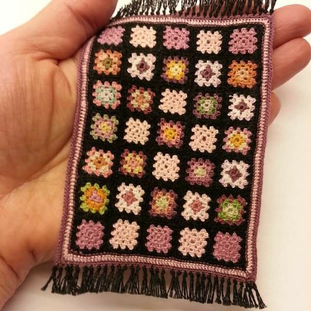 a hand holding a small black and pink crocheted square with flowers on it