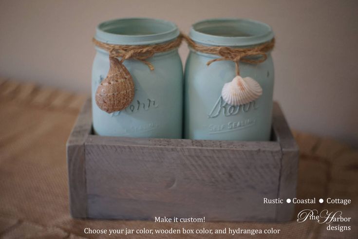 two blue mason jars with seashells are sitting in a wooden box on a bed