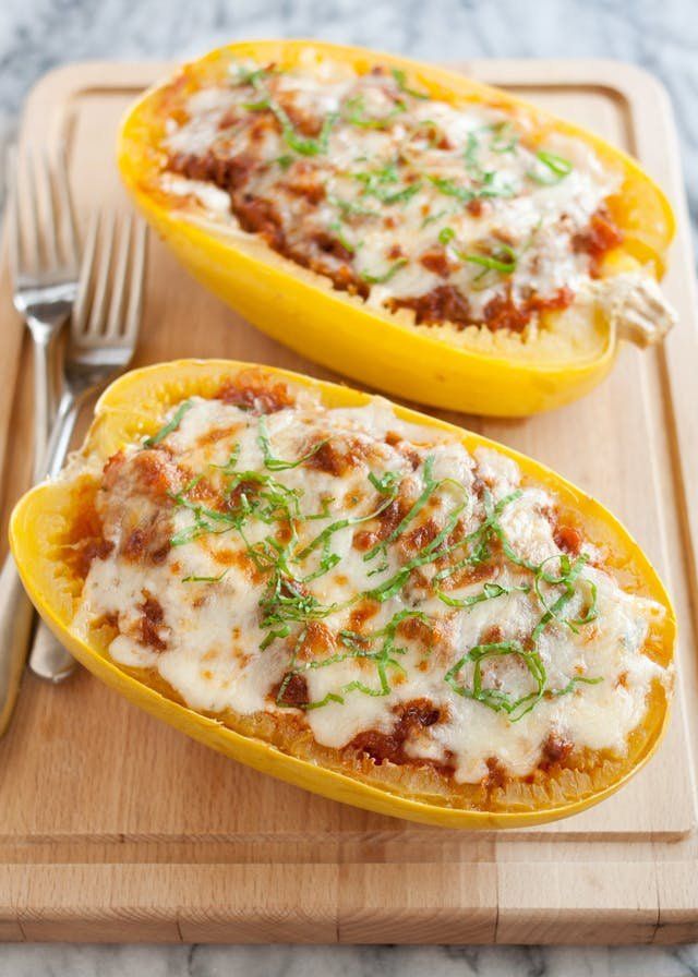 two stuffed yellow peppers with cheese and herbs on a cutting board next to a fork