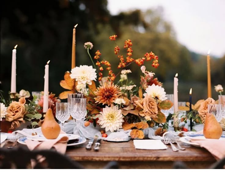 a table set with flowers and candles for an outdoor dinner party in the fall or winter