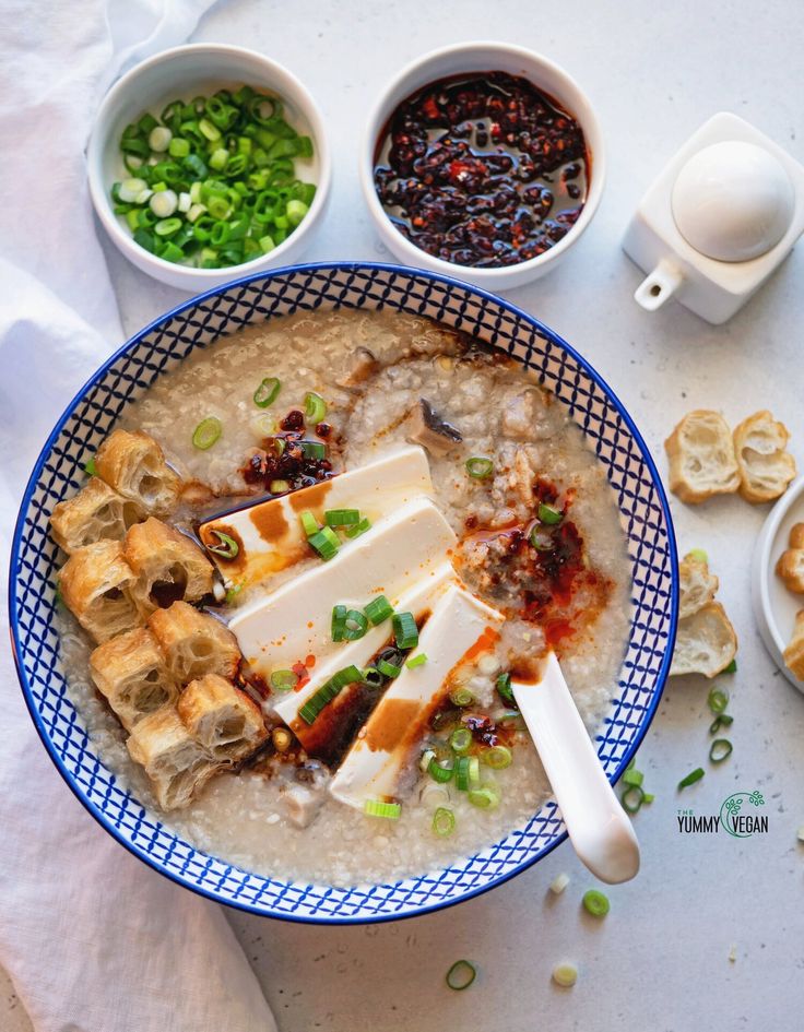 a bowl of oatmeal topped with tofu and green onions next to bowls of other foods