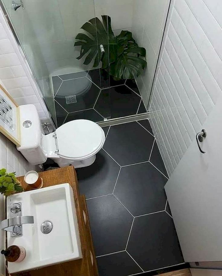 a small bathroom with a toilet, sink and shower stall in the corner next to a potted plant