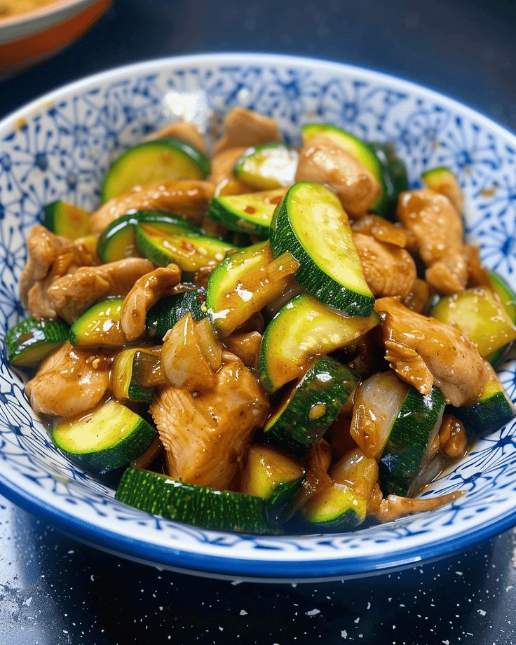 a blue and white bowl filled with cucumbers, chicken and sesame seed sauce