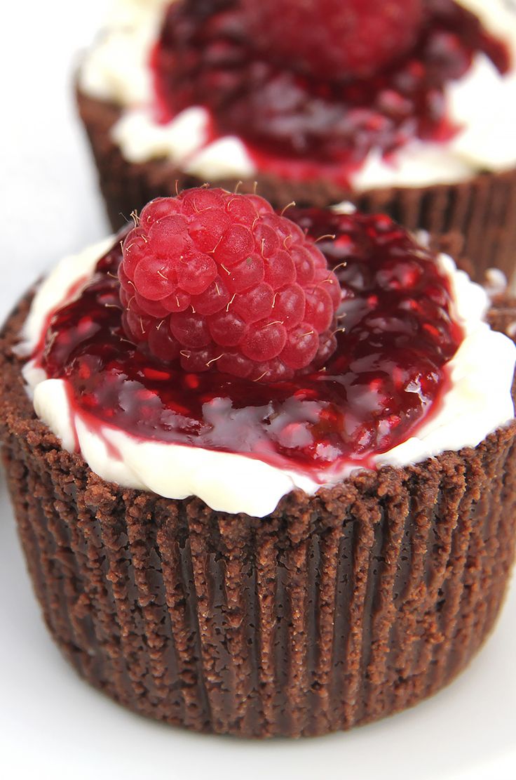 two chocolate cupcakes with raspberries and cream frosting on white background