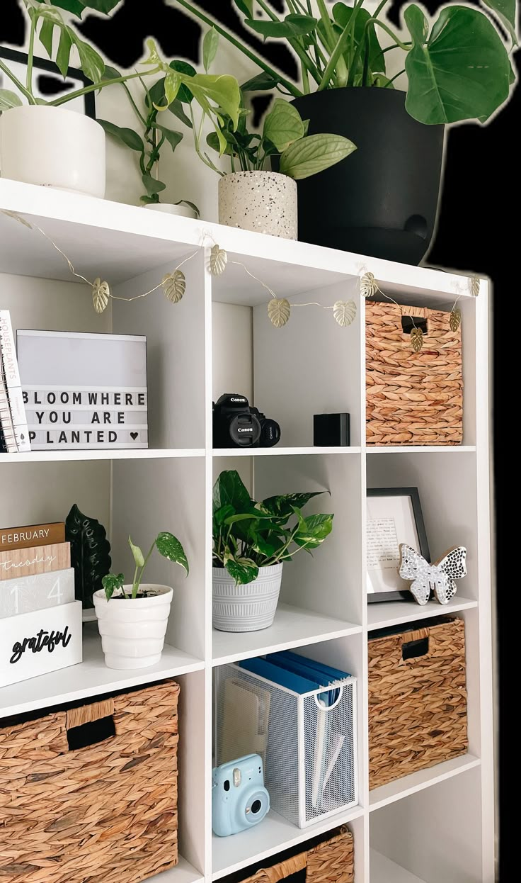 a white bookcase with baskets and plants on the top, along with other items