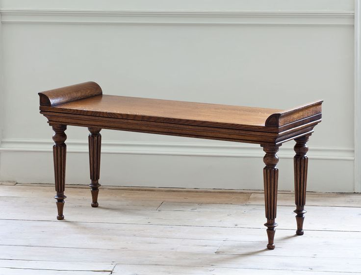 a wooden bench sitting on top of a hard wood floor next to a white wall