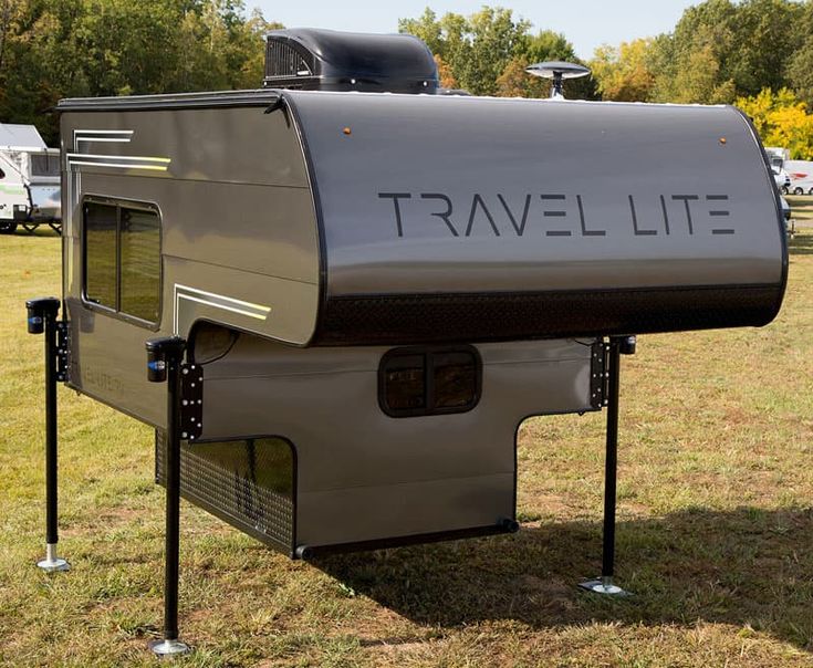 a travel lite trailer parked in the grass with trees in the backgroud