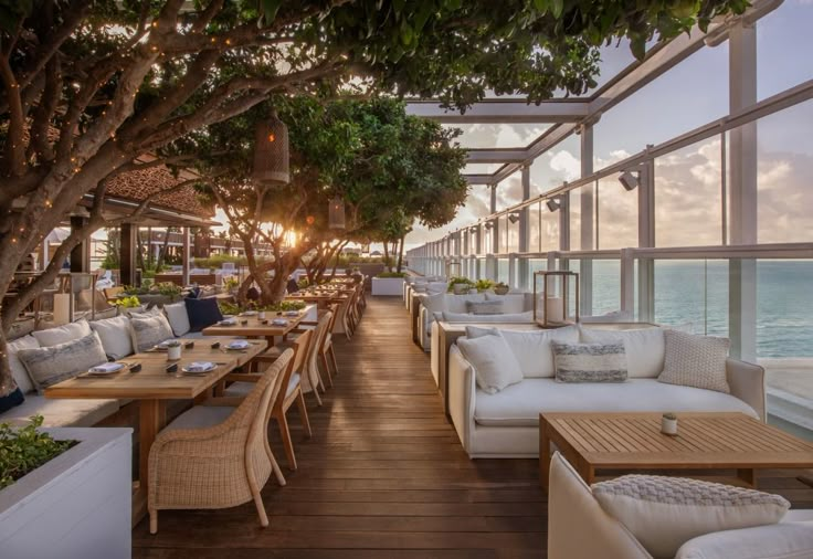 an outdoor dining area overlooking the ocean with tables, chairs and couches set up