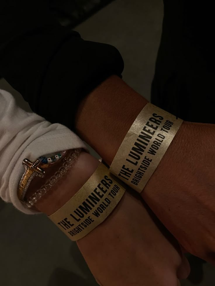 two people wearing gold bracelets with words on them