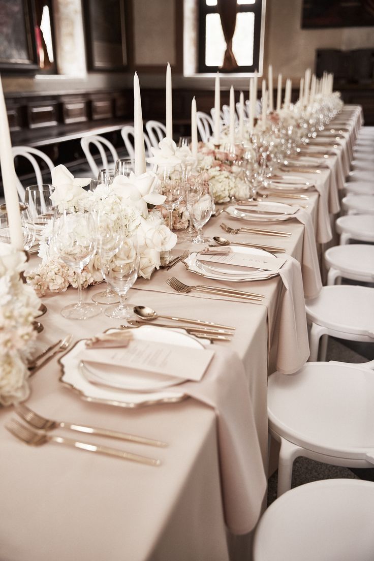 a long table with white flowers and silverware is set for an elegant dinner party