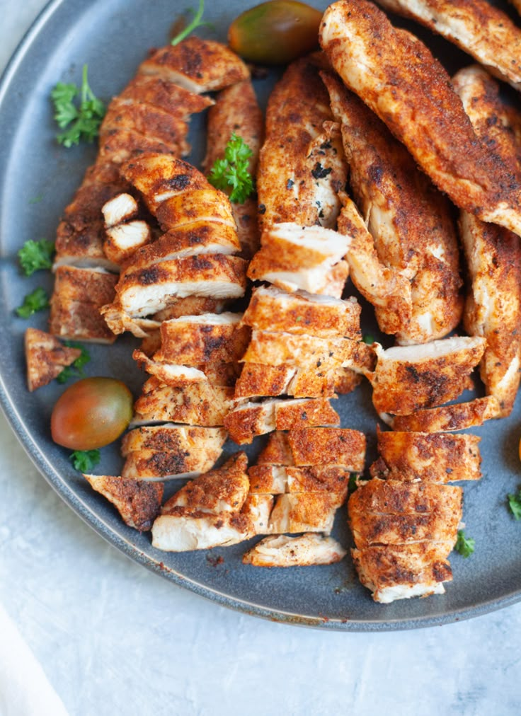 grilled chicken tenders on a plate with tomatoes and parsley in the background