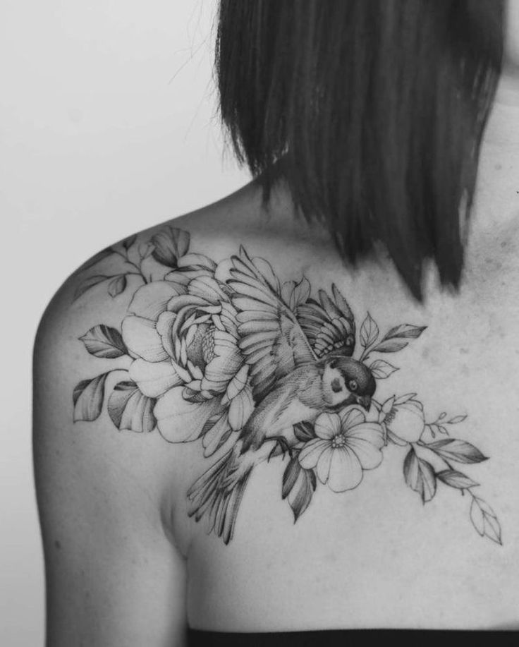 the back of a woman's shoulder with flowers and a bird tattoo on it