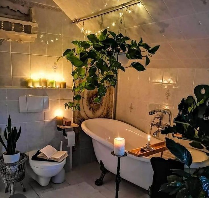 the bathroom is decorated in white and has potted plants on the wall, while candles are lit next to the tub