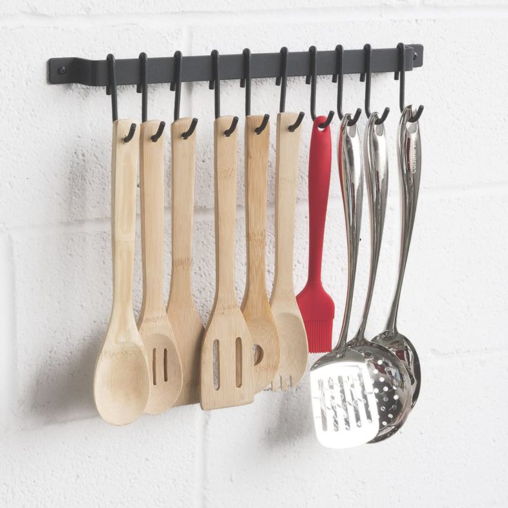 wooden utensils hanging on a wall with black hooks and red spatulas