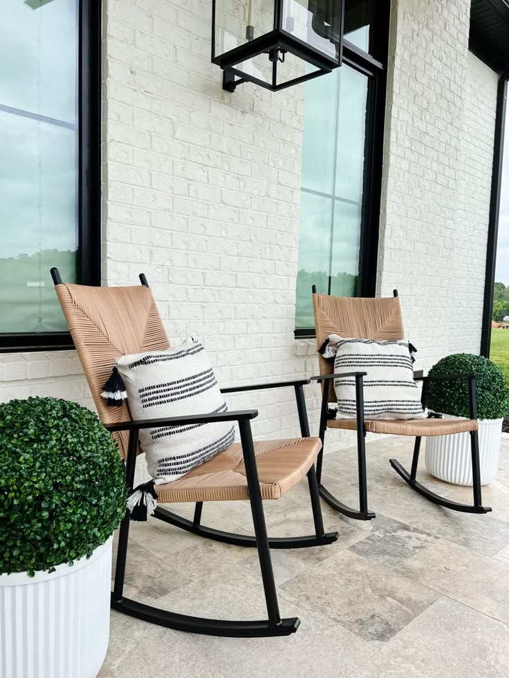 two wooden rocking chairs sitting on top of a stone floor next to a white brick building