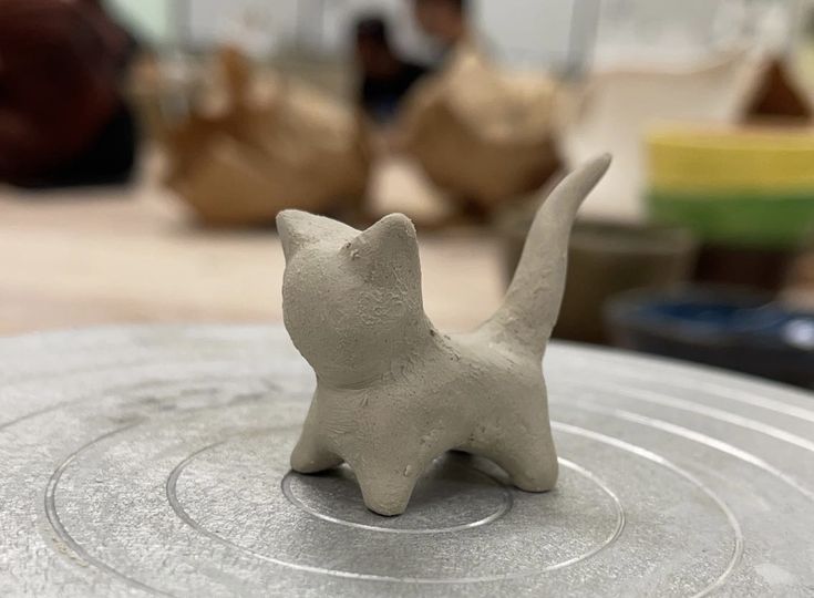 a small white cat figurine sitting on top of a metal object in a room