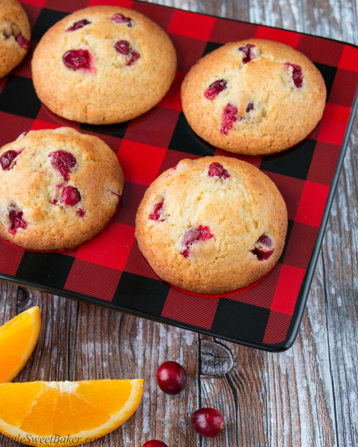 muffins with cranberries on a red and black tray next to an orange slice