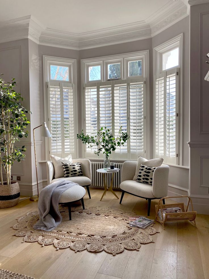 a living room filled with furniture and windows covered in white shuttered shades on top of them