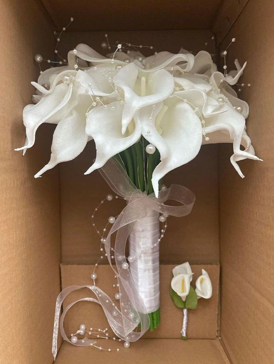 a bouquet of white flowers in a cardboard box with ribbons and pearls on the side