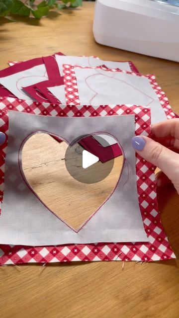 someone is making a heart out of paper on top of red and white checkered fabric