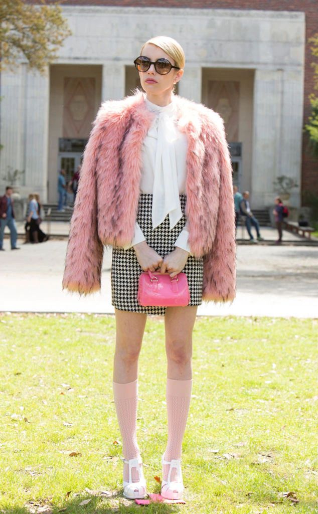 a woman standing on top of a lush green field wearing a pink coat and skirt