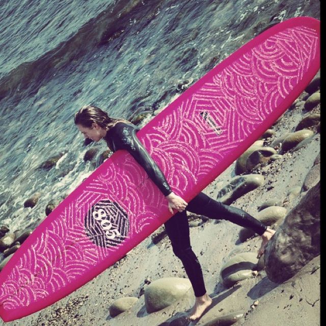 a woman holding a pink surfboard on top of a beach