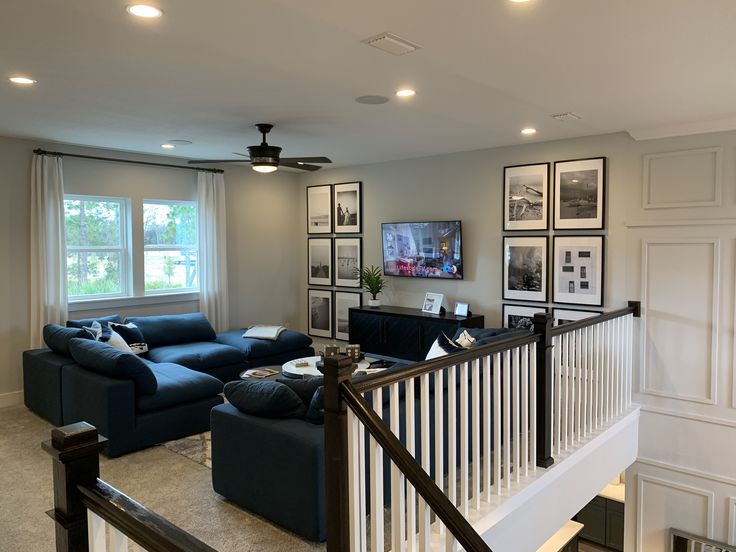 a living room with blue couches and pictures on the wall next to stairs in front of windows