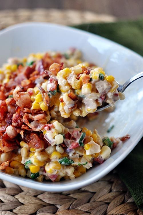 a spoon with some food on it in a white bowl next to another plate filled with corn