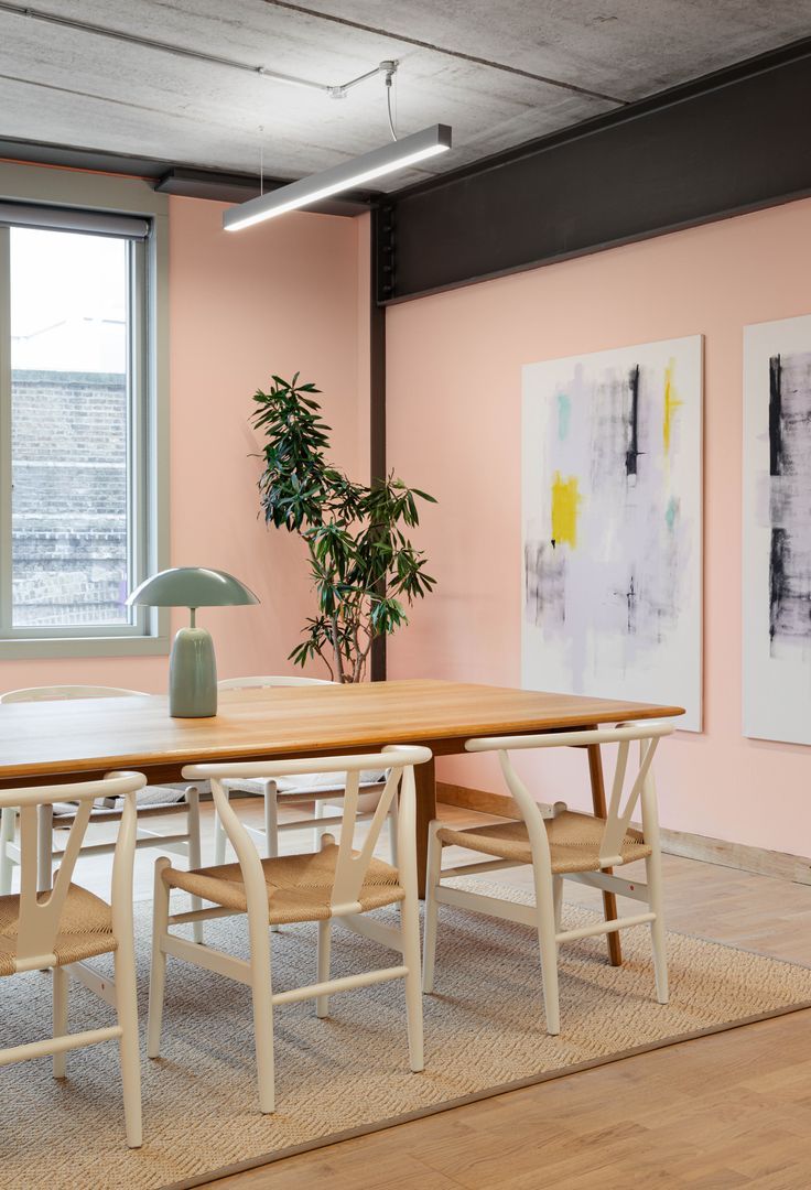 an office with pink walls and wooden tables in front of a large painting on the wall