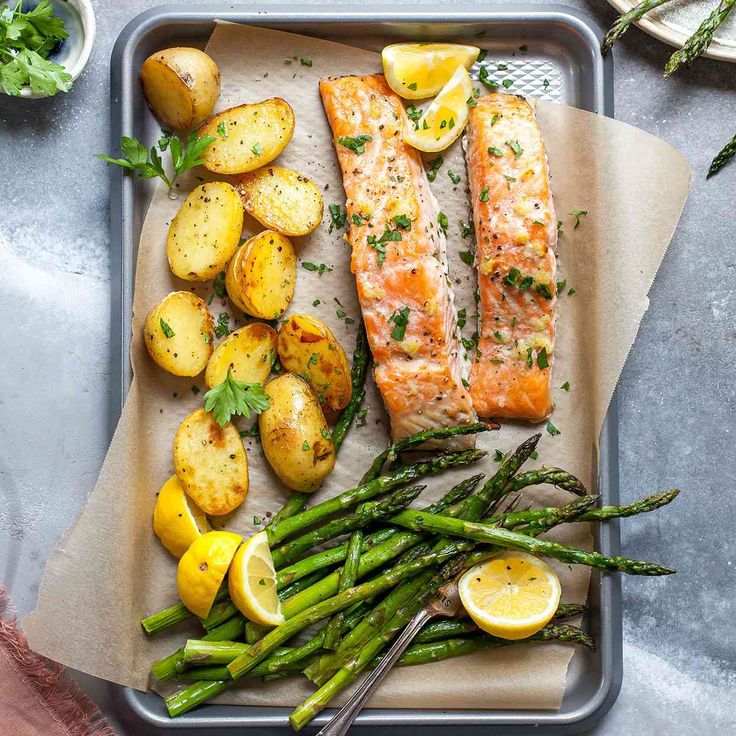 salmon and asparagus on a tray with lemons, potatoes and parsley