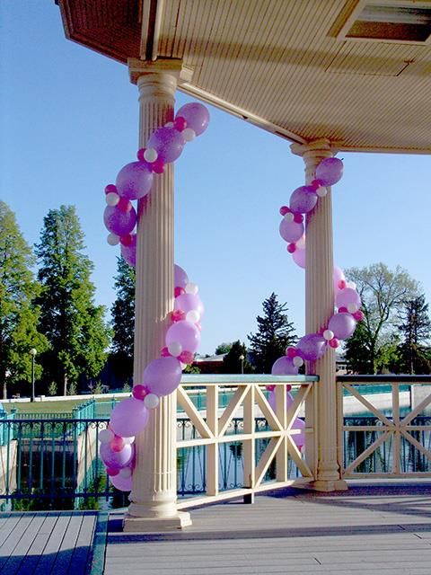 some pink and white balloons are hanging from the ceiling over a wooden deck near water