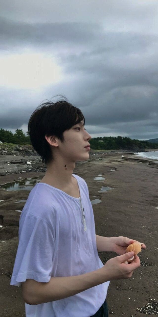 a man standing on top of a beach next to the ocean holding a piece of food