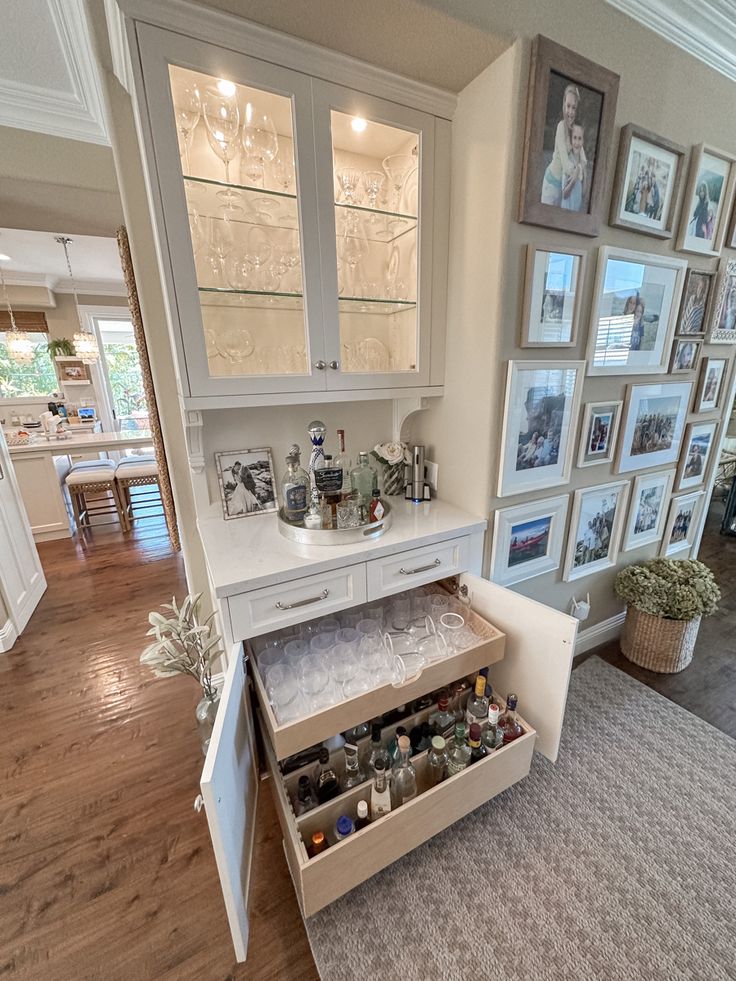 an open cabinet in the middle of a living room with pictures on the wall behind it