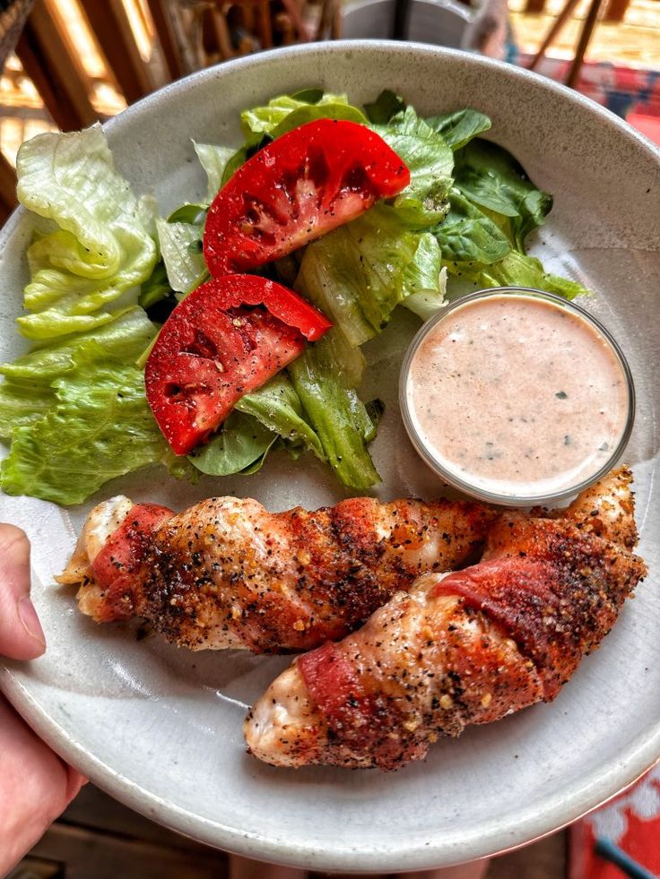 a white plate topped with chicken, lettuce and tomato slices next to a salad