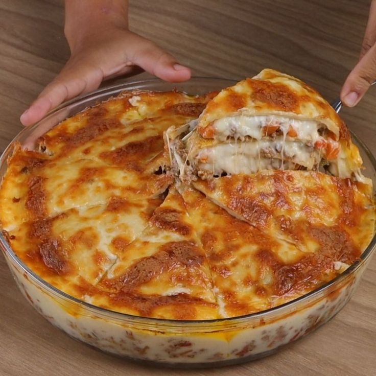 a person holding a pizza in their hand over a casserole dish on a wooden table