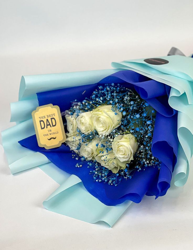 a bouquet of white roses in blue paper with a tag on it that says dad