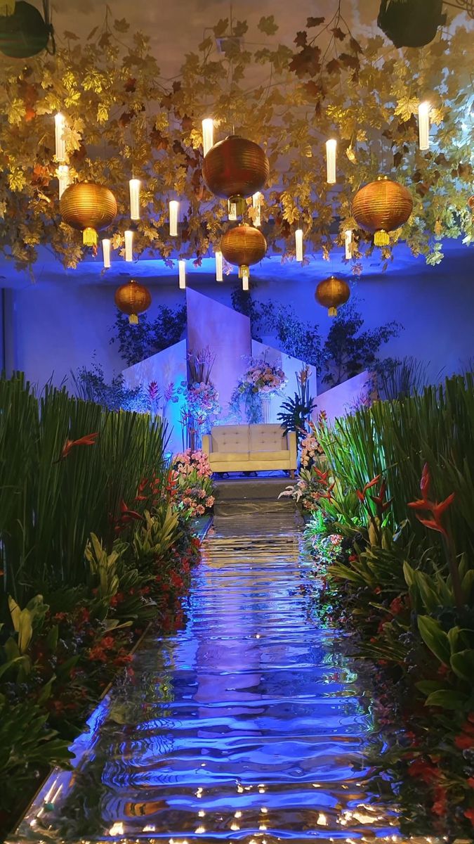 the inside of a building with plants and lights hanging from it's ceiling over water