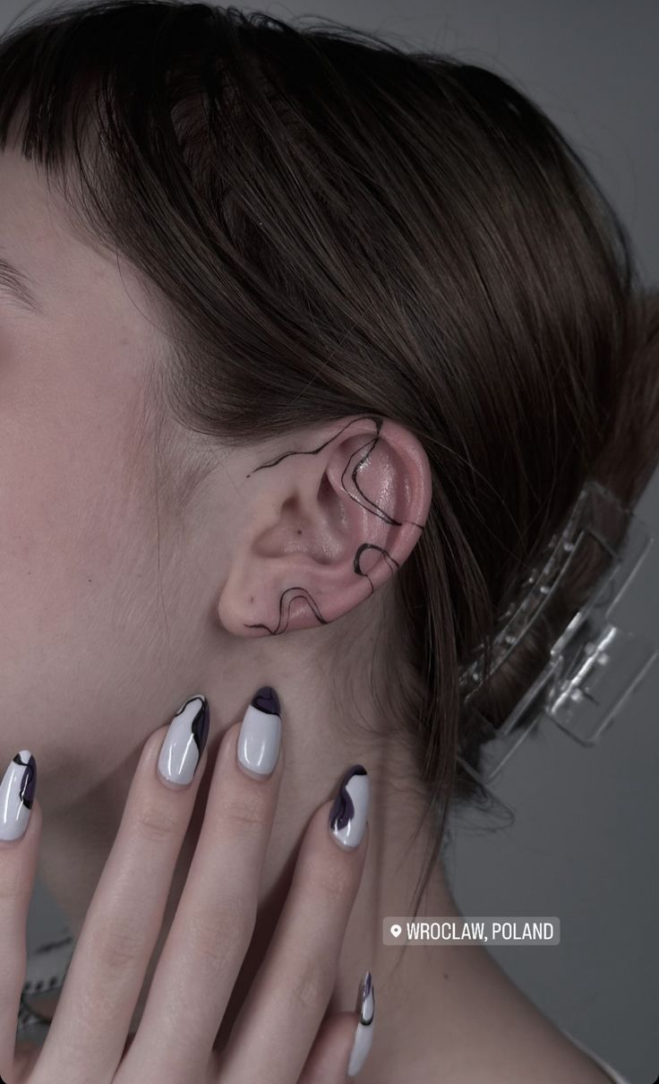 a woman with black and white nail polish holding her ear up to the side while she is