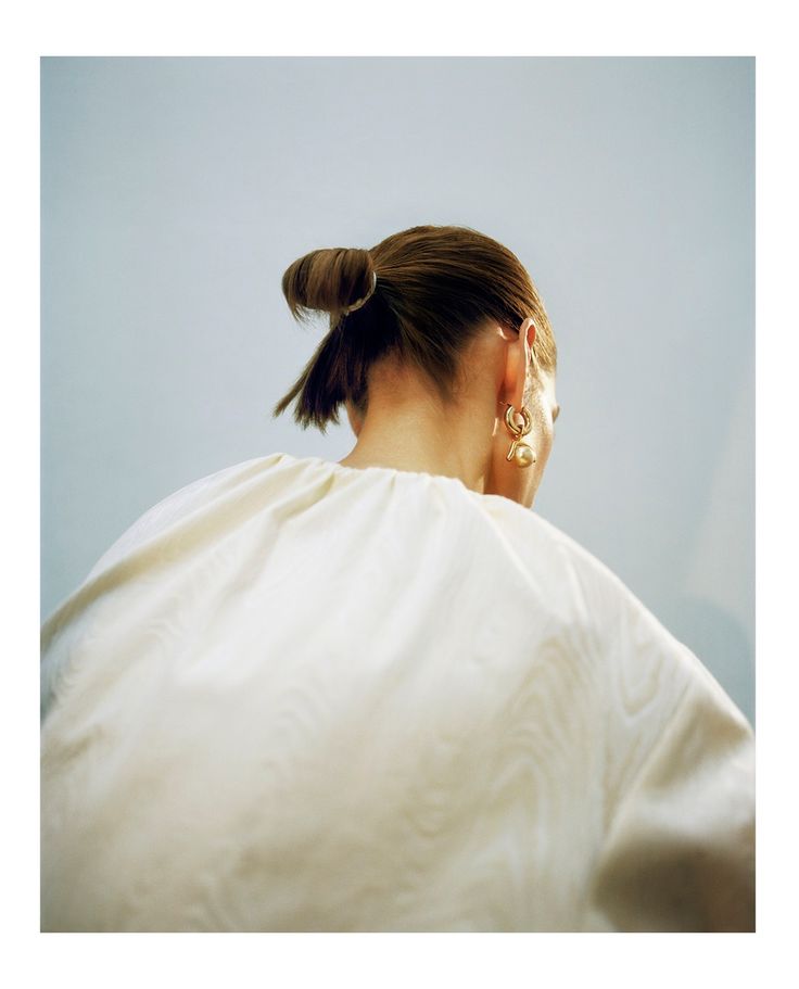 a woman with her hair in a bun wearing a white shirt and gold earrings